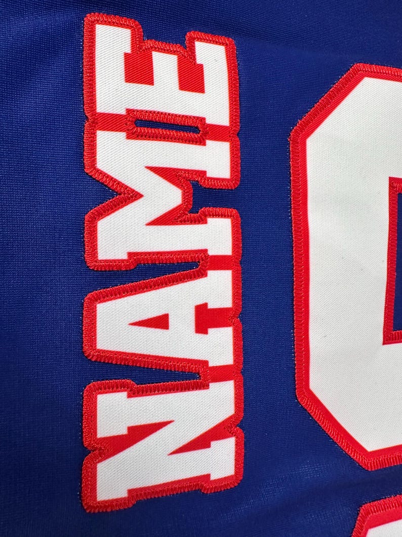 May include: White jersey with red stitching, the word "NAME" is sewn on the front in white letters with red outlines.