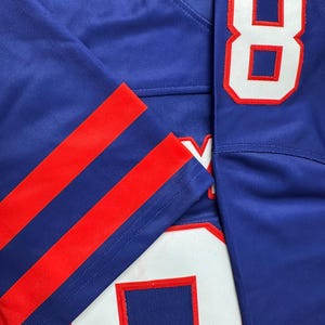 May include: A blue jersey with red and white stripes on the sleeves. The jersey has the number "8" on the right side and the number "0" on the left side.