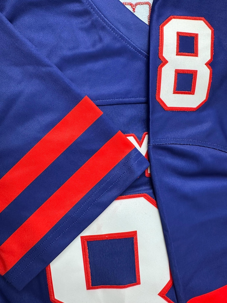 May include: A blue jersey with red and white stripes on the sleeves. The jersey has the number "8" on the right side and the number "0" on the left side.
