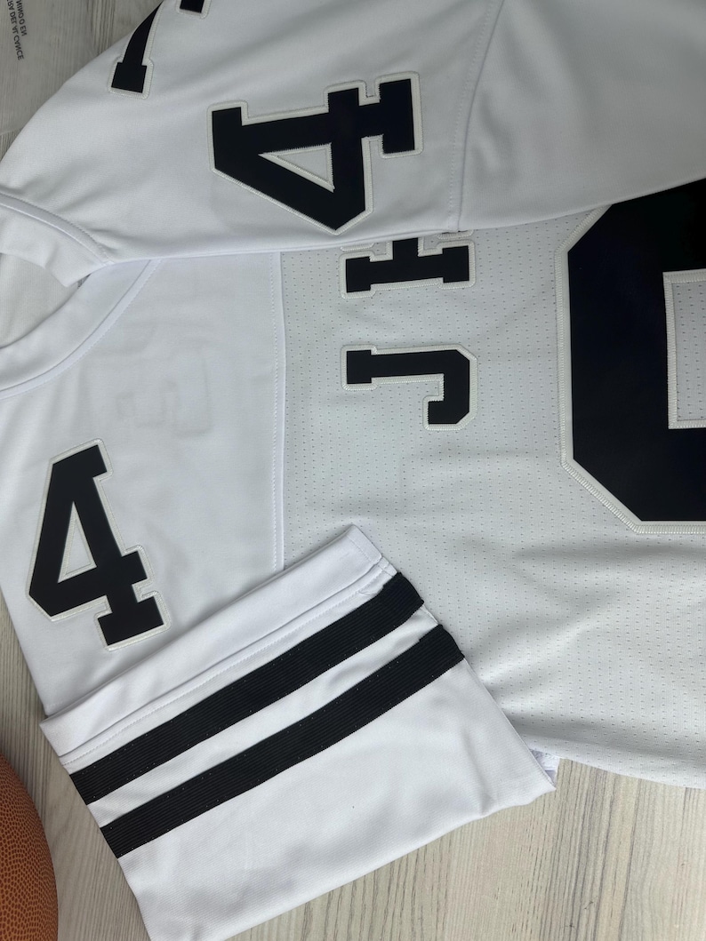 Pu&ograve; includere: Maglia bianca con doppie strisce nere sulle maniche. La maglia ha un numero nero "4" sul davanti e un numero nero "4" sulla manica sinistra. La maglia ha anche una lettera nera "J" e un numero nero "4" sul retro.