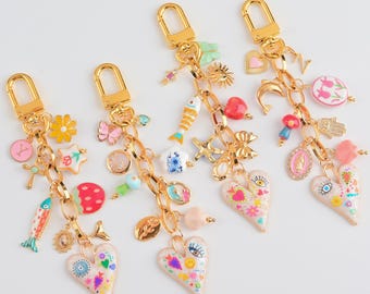May include: Four gold-tone keychains with various charms, including hearts, fish, flowers, and religious symbols. The charms are in various colors, including pink, yellow, blue, and red. Each keychain has a heart-shaped charm with colorful designs.