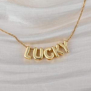 Könnte beinhalten: Goldkette mit dem Wort "LUCKY" in einzelnen Buchstaben.