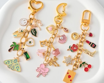 May include: Three gold-toned keychains with various charms. Charms include a smiley face, a green leaf, a heart, a butterfly, a palm tree, a pink bow, a star, a seashell, a rose, a lipstick, a boot, a playing card, and cherries.