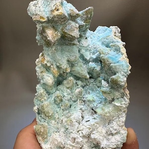 May include: A natural mineral specimen featuring a cluster of crystals. The crystals have a light blue and tan color palette, with a rough, textured surface. The mineral is a unique geological formation.