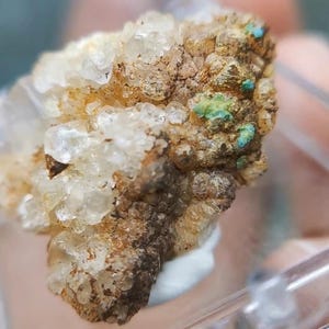 May include: A raw mineral specimen featuring a cluster of translucent, pale yellow crystals attached to a textured, brownish-tan rock matrix. Small, vibrant turquoise-colored mineral deposits are visible on the surface of the rock.