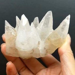 May include: A cluster of translucent, white, and pale yellow crystalline points forming a jagged, crown-like structure. The mineral specimen features multiple sharp, pointed peaks with a glassy, semi-transparent texture and visible internal fractures.
