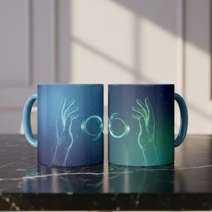 May include: Two ceramic mugs featuring a gradient blue and green background. Each mug displays a glowing, ethereal hand reaching toward a central, luminous infinity symbol. The design incorporates light particles and soft, flowing lines.