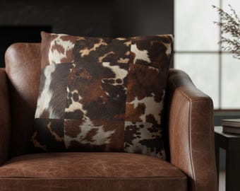 May include: A square throw cushion featuring a patchwork design of brown, white, and black cowhide patterns. The cushion displays various animal hide textures arranged in a grid-like composition, showcasing natural mottled spots and hair-like details.
