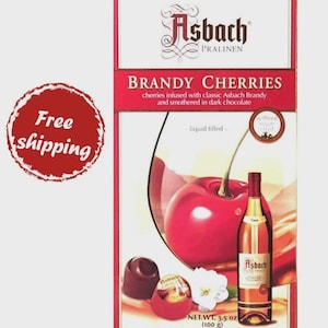 May include: A red and white box of Asbach Brandy Cherries. The box features a graphic of a cherry, a bottle of brandy, and a chocolate candy. The text on the box reads "BRANDY CHERRIES" and "cherries infused with classic Asbach Brandy and smothered in dark chocolate."