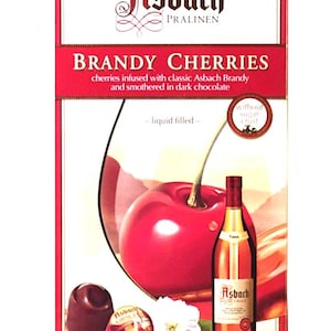 May include: Box of Asbach Brandy Cherries. The packaging features a large red cherry, a bottle of Asbach brandy, and a chocolate candy. The text reads "BRANDY CHERRIES" and "cherries infused with classic Asbach Brandy and smothered in dark chocolate". Net weight is 3.5 oz.