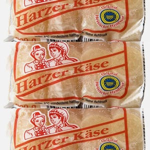 May include: Three packages of Harzer Käse, a German cheese, with a red and white label featuring a couple in traditional clothing. The label also includes the text "Harzer Käse" and "Original Hessischer Handkäse".