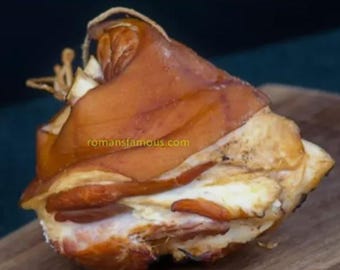 May include: A close-up of a roasted pork knuckle, with a crispy brown skin and a light brown interior. The knuckle is sitting on a wooden cutting board.