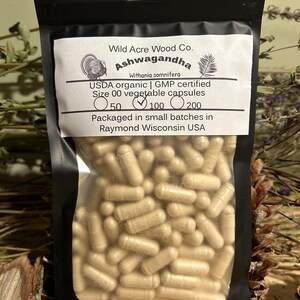 May include: A clear plastic bag filled with beige capsules labeled "Wild Acre Wood Co. Ashwagandha Withania somnifera USDA organic | GMP certified Size 00 vegetable capsules 50 100 200 Packaged in small batches in Raymond Wisconsin USA"