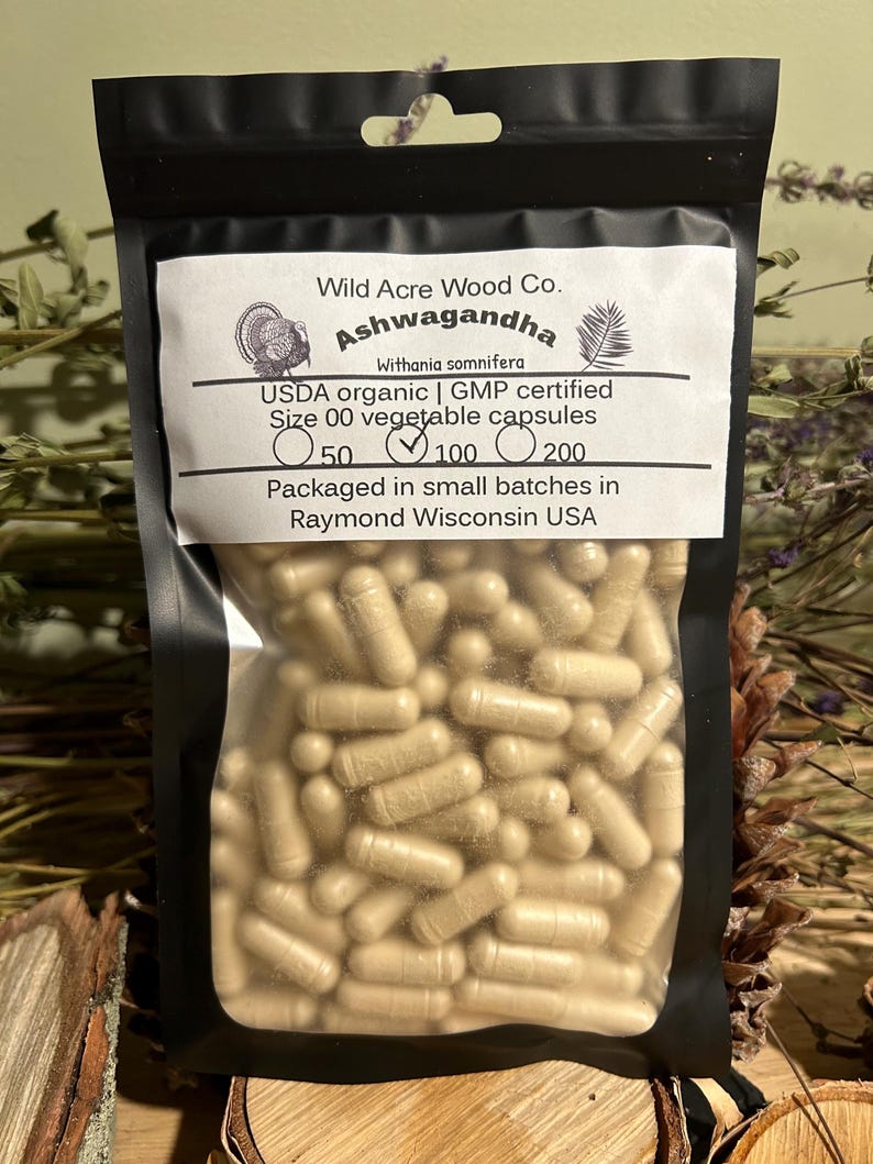 May include: A clear plastic bag filled with beige capsules labeled "Wild Acre Wood Co. Ashwagandha Withania somnifera USDA organic | GMP certified Size 00 vegetable capsules 50 100 200 Packaged in small batches in Raymond Wisconsin USA"