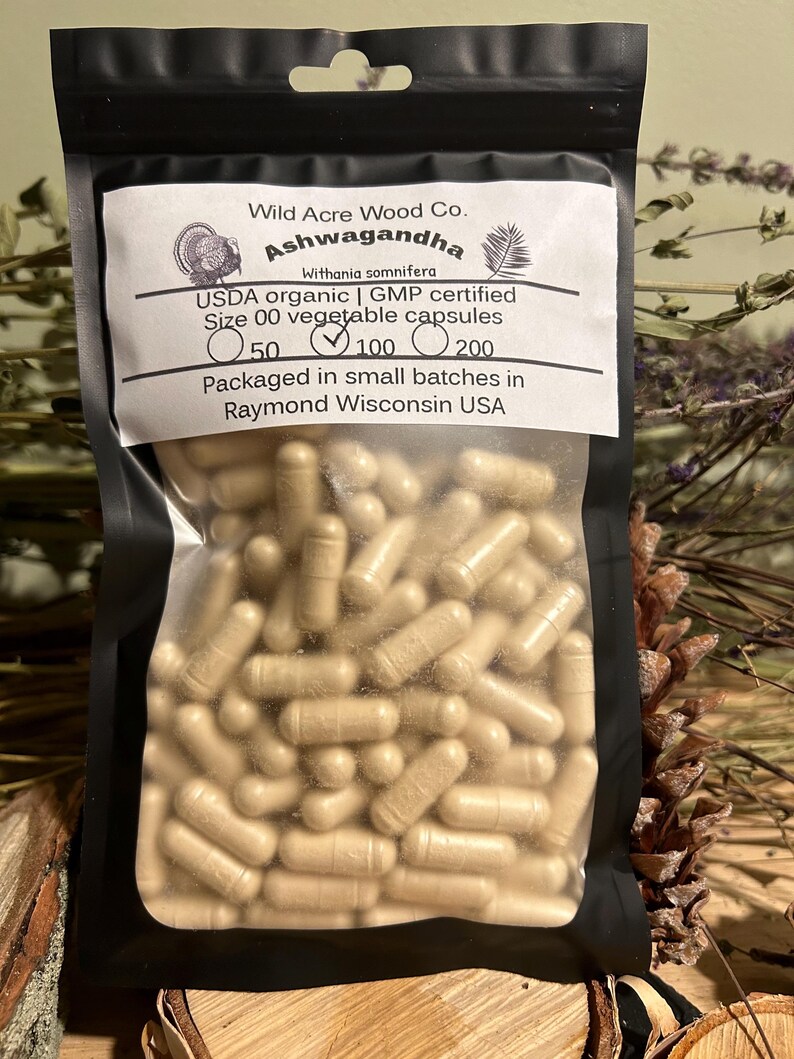 May include: A black resealable bag with a white label that reads "Wild Acre Wood Co. Ashwagandha Withania somnifera USDA organic | GMP certified Size 00 vegetable capsules 50 100 200 Packaged in small batches in Raymond Wisconsin USA". The bag contains a large quantity of beige capsules.