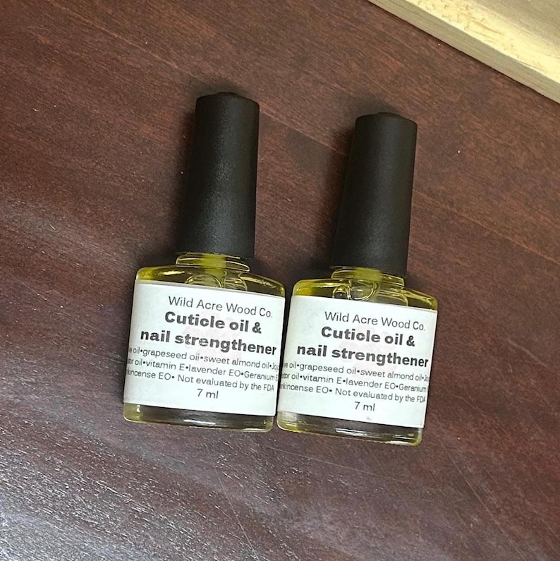 May include: Two 7 ml bottles of cuticle oil and nail strengthener by Wild Acre Wood Co. The bottles are clear and contain a yellow liquid. The labels are white with black text and list the ingredients: grapeseed oil, sweet almond oil, vitamin E, lavender EO, geranium, and incense EO. The bottles are not evaluated by the FDA.