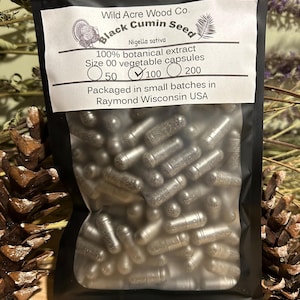 May include: A black resealable bag with a white label that reads "Wild Acre Wood Co. Black Cumin Seed Nigella sativa 100% botanical extract Size 00 vegetable capsules 50 100 200 Packaged in small batches in Raymond Wisconsin USA". The bag contains silver capsules.