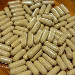 Peut inclure: Un bol rempli d'une grande quantit&eacute; de capsules brunes. Les capsules sont translucides et remplies d'une poudre brun clair.