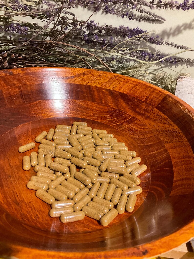 May include: A collection of numerous light brown, cylindrical capsules filled with a granular substance, resting inside a polished, dark reddish-brown wooden bowl with a visible grain pattern and a smooth, rounded interior surface.