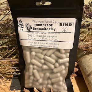 May include: A black pouch filled with size 00 vegetable capsules. The pouch has a white label with the text "Wild Acre Wood Co. FOOD GRADE Bentonite Clay" and "Made in the USA | 100% pure". The label also indicates the quantity of capsules: 50, 100, or 200.