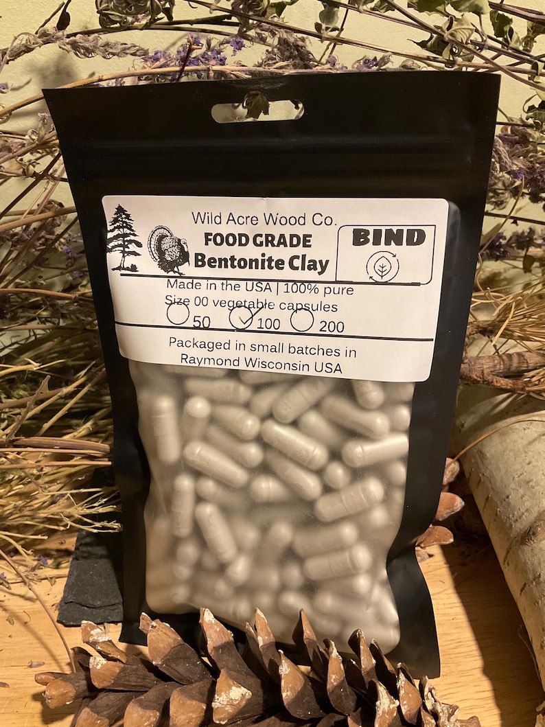 May include: A black pouch filled with size 00 vegetable capsules. The pouch has a white label with the text "Wild Acre Wood Co. FOOD GRADE Bentonite Clay" and "Made in the USA | 100% pure". The label also indicates the quantity of capsules: 50, 100, or 200.