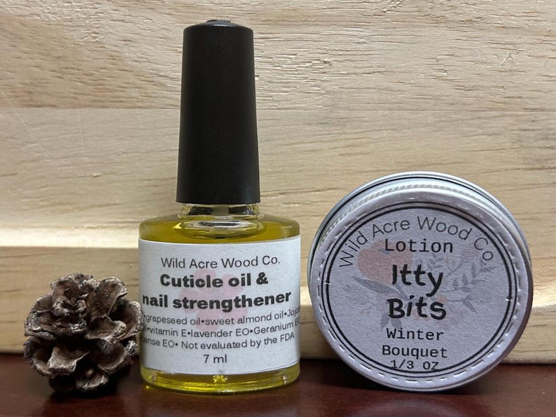 May include: Two small bottles of beauty products. A clear glass bottle with a black cap contains cuticle oil and nail strengthener. A silver tin contains a lotion called "Itty Bits Winter Bouquet".