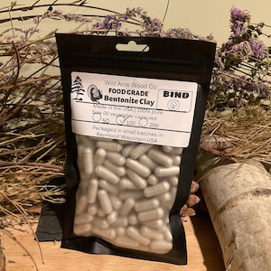 May include: A black pouch containing Bentonite Clay capsules. The label reads "Wild Acre Wood Co. FOOD GRADE Bentonite Clay." The capsules are size 00 vegetable capsules, with options for 50, 100, or 200 capsules per bag. Made in the USA.