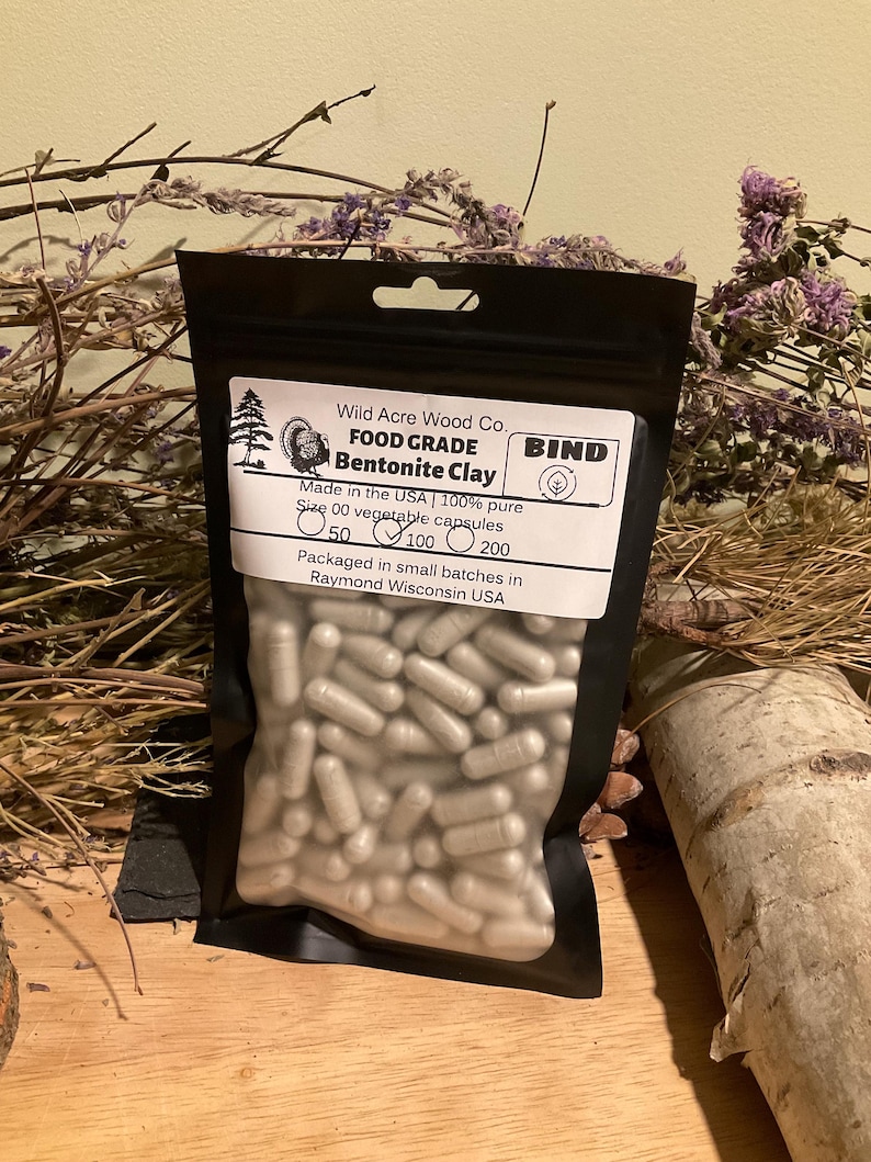 May include: A black pouch containing Bentonite Clay capsules. The label reads "Wild Acre Wood Co. FOOD GRADE Bentonite Clay." The capsules are size 00 vegetable capsules, with options for 50, 100, or 200 capsules per bag. Made in the USA.