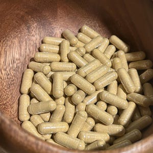 Peut inclure: Un bol en bois rempli d'une grande quantit&eacute; de capsules transparentes contenant une poudre brun clair.