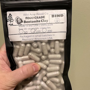 May include: A black bag filled with size 00 vegetable capsules of Bentonite Clay. The bag has a white label with the text "Wild Acre Wood Co. FOOD GRADE Bentonite Clay" and "Made in the USA". The bag contains 100 capsules.