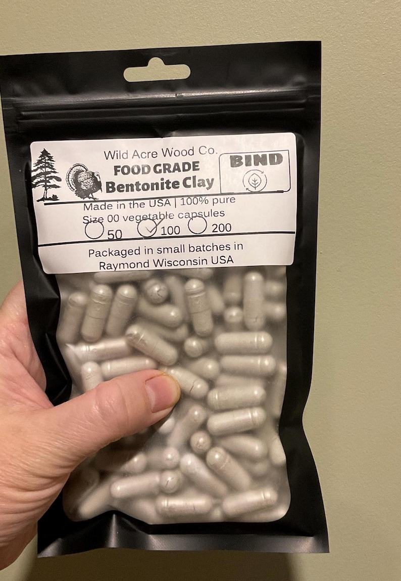 May include: A black bag filled with size 00 vegetable capsules of Bentonite Clay. The bag has a white label with the text "Wild Acre Wood Co. FOOD GRADE Bentonite Clay" and "Made in the USA". The bag contains 100 capsules.