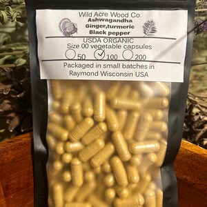 Peut inclure: Un sac en plastique transparent rempli d'une grande quantit&eacute; de capsules jaunes dor&eacute;es. Le sac est &eacute;tiquet&eacute; "Wild Acre Wood Co. Ashwagandha Gingembre, curcuma Poivre noir USDA ORGANIC Taille 00 capsules v&eacute;g&eacute;tales 50 100 200 Conditionn&eacute; en petits lots &agrave; Raymond Wisconsin USA"