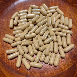 Peut inclure: Un bol en bois rempli d'une grande quantit&eacute; de capsules brunes. Les capsules sont translucides et semblent &ecirc;tre remplies d'une poudre brune.