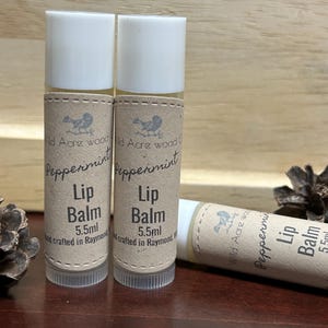 Absolutely perfect 100% natural organic lip balms perfect for the time of year ahead of us!  WINTER! To lip balms stand upright, one is lying down with two scotch pine cones in the background.quench your thirsty lips with this moisturizing lip balm.