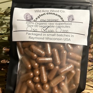 May include: A resealable bag filled with brown capsules labeled "Wild Acre Wood Co. Ceylon Cinnamon RAW ORGANIC 100% Organic raw superfood Size 00 vegetable capsules 50 100 200 Packaged in small batches in Raymond Wisconsin USA"
