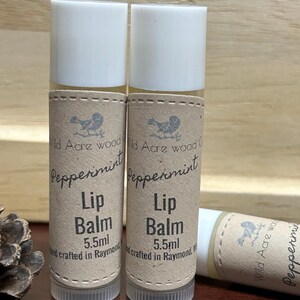May include: Two brown and white tubes of peppermint lip balm, each with a label that reads "Wild Acre Wood Crafts Peppermint Lip Balm 5.5ml and crafted in Raymond, WA".