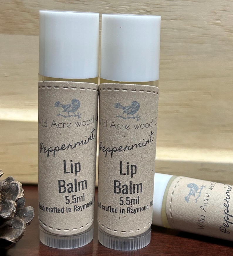 May include: Two brown and white tubes of peppermint lip balm, each with a label that reads "Wild Acre Wood Crafts Peppermint Lip Balm 5.5ml and crafted in Raymond, WA".