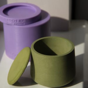 May include: Two containers with lids, one is purple and the other is green. The green container has a lid that is slightly ajar.