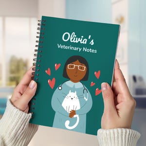 May include: A teal spiral-bound notebook with the text "Olivia's Veterinary Notes." The cover features an illustration of a veterinarian with a stethoscope, holding a white cat, surrounded by red hearts.