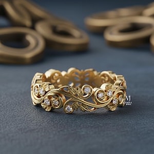 以下が含まれることがあります： 金色のリングで、花の模様と小さな透明な宝石が付いています。 リングは葉と渦の複雑なパターンを特徴とし、宝石はデザイン全体にセットされています。 リングは濃い青色の表面にあります。