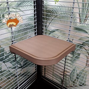 May include: A brown corner shelf for a bird cage. The shelf is made of a smooth, rounded plastic and is attached to the cage with two metal clips.