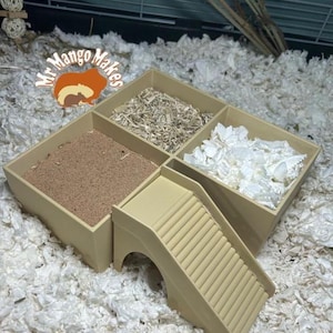 Peut inclure: Une mangeoire en plastique beige à plusieurs compartiments avec une rampe et un tunnel pour petits animaux. La mangeoire comporte trois compartiments remplis de différents types de litière. La mangeoire est posée sur un lit de papier blanc déchiqueté.