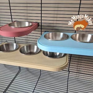 May include: Three pet food dishes in pink, light blue, and beige, each with stainless steel bowls. The dishes are mounted on a wire cage. The top right corner has a logo that says "Mr. Mango Makes" with a cartoon squirrel.