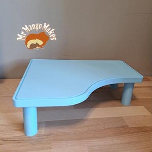 May include: A light blue, small, rectangular table with rounded corners and four cylindrical legs. The table has a curved edge on one side. The logo "Mr Mango Makes" is visible in the background.