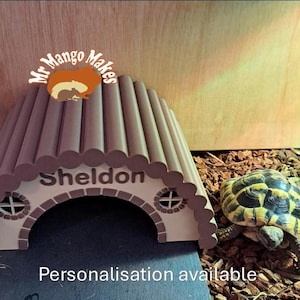 May include: A brown tortoise shell with a personalised archway hide for a small reptile. The archway is labelled "Sheldon" and has a logo that says "Mr. Mango Makes".