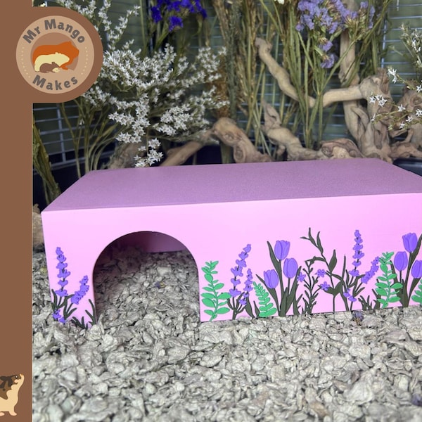 May include: A pink hamster house with a rounded entrance and floral decorations. The house features purple tulips and lavender sprigs along the front. The Mr. Mango Makes logo is visible in the upper left corner.