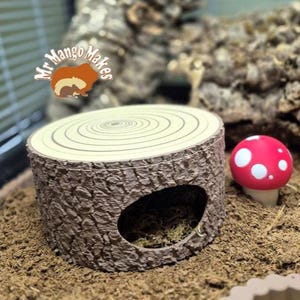 May include: A decorative habitat accessory featuring a tree stump hideout with a circular top and a side opening. A red mushroom with white spots sits nearby. The logo "Mr Mango Makes" is visible.