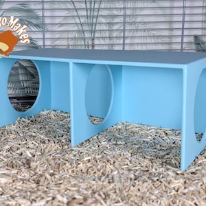 May include: A light blue wooden tunnel with three openings, designed for small animals. The tunnel is made of plywood and has a smooth finish. It is sitting on a bed of wood shavings.