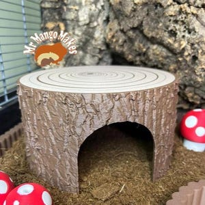 May include: A brown, tree stump-shaped pet habitat with a circular top and a hollowed-out centre. The habitat has a textured bark-like exterior and a small arched entrance. The habitat is surrounded by brown bedding and red mushroom decorations.