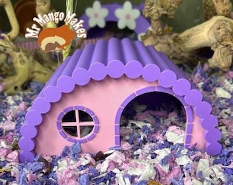 May include: A pink and purple hamster house with a scalloped roof and a round window. The house has an arched doorway and is surrounded by colorful bedding. The image includes the text "Mr Mango Makes".
